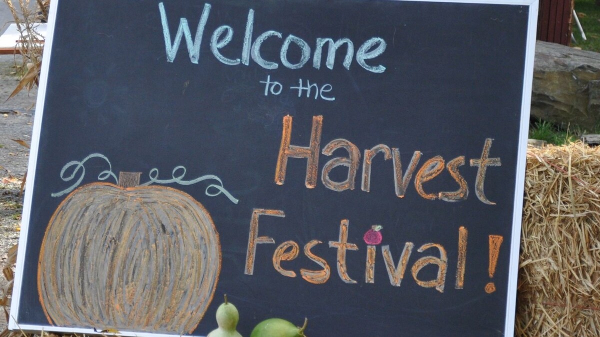A chalkboard sign propped on hay bales reading Welcome to Harvest Festival